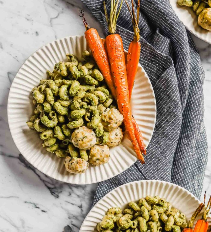 Photograph of three plates filled with carrot top pesto pasta, roasted carrots and chicken meatballs