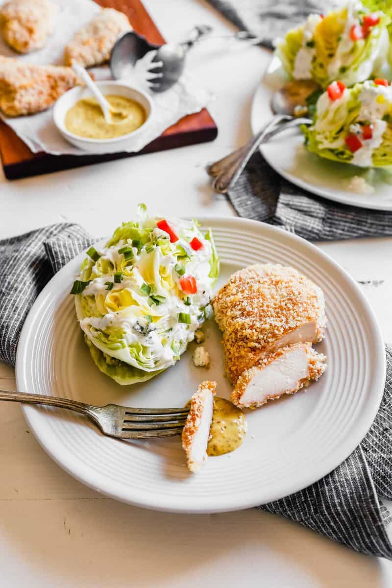 Photograph of oven fried chicken breast being cut on a plate with a wedge salad
