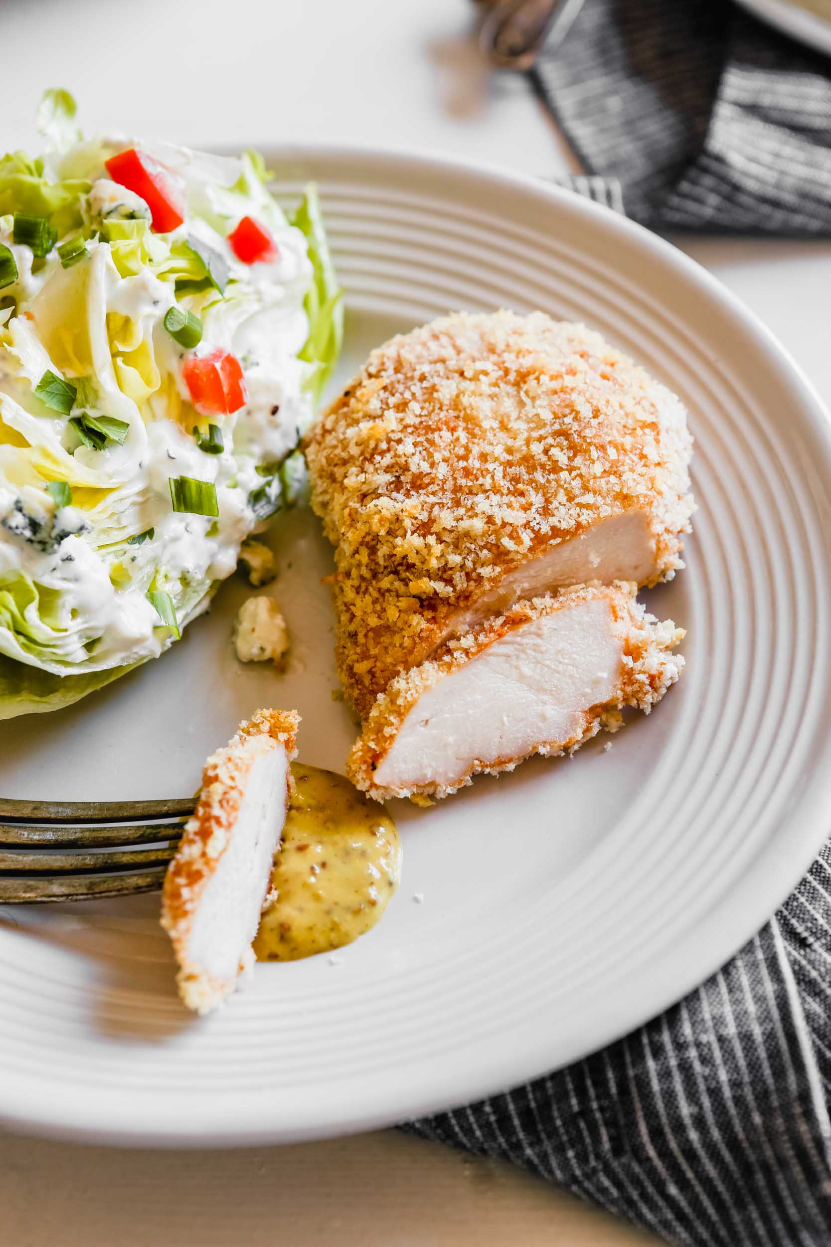 Photograph of oven fried chicken breast being cut on a plate with a wedge salad