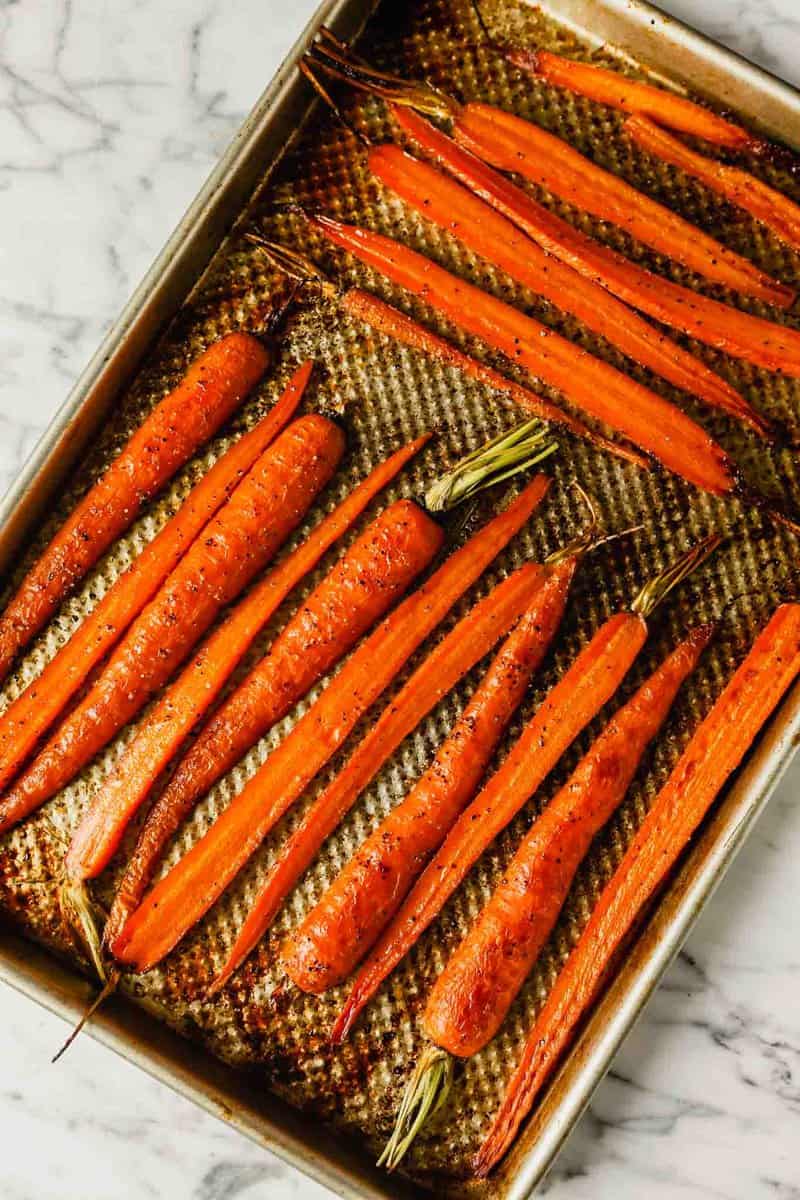 Photograph of roasted halved carrots on a baking sheet