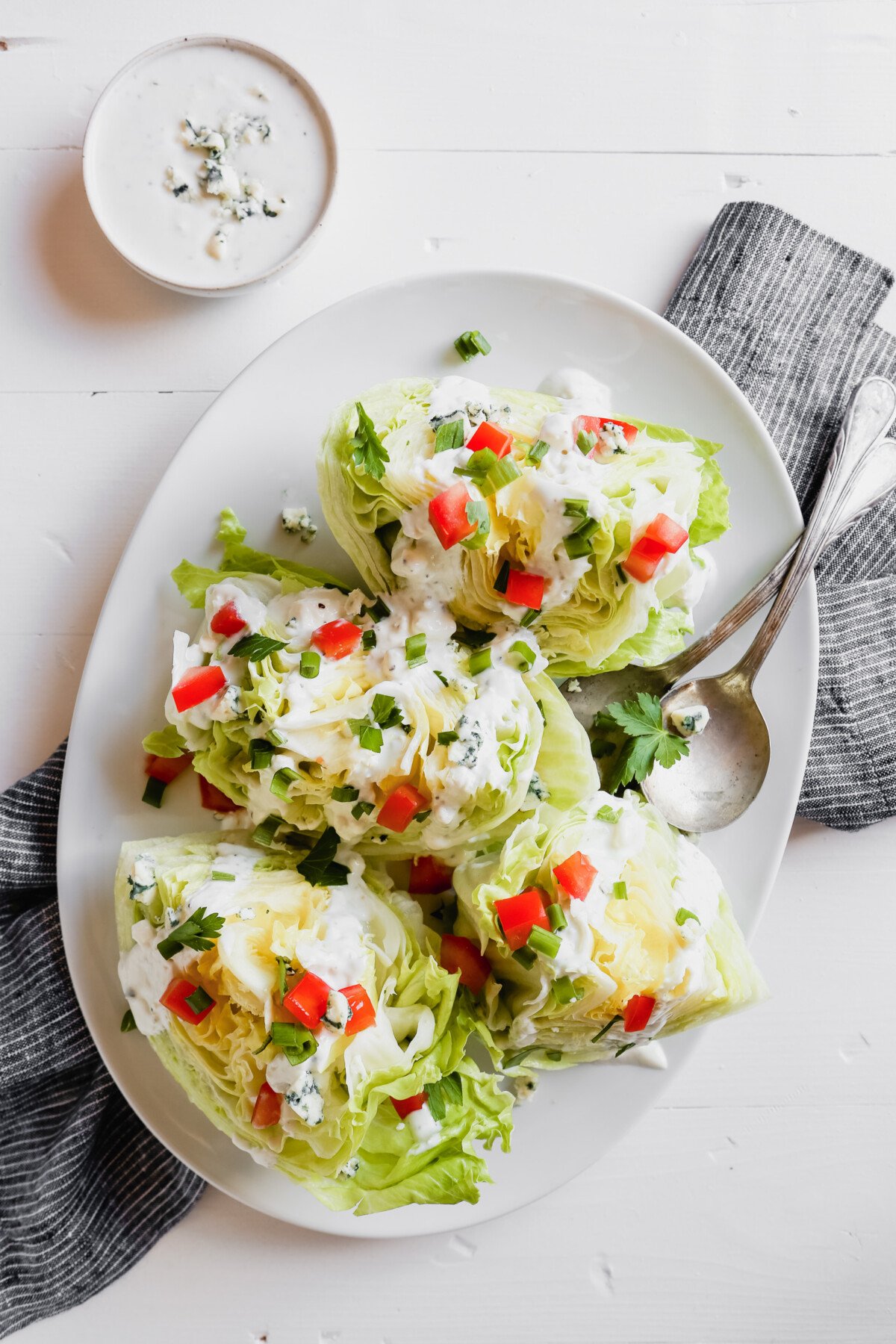 Photograph of a wedge salad with blue cheese dressing on a white plate set on a marble table