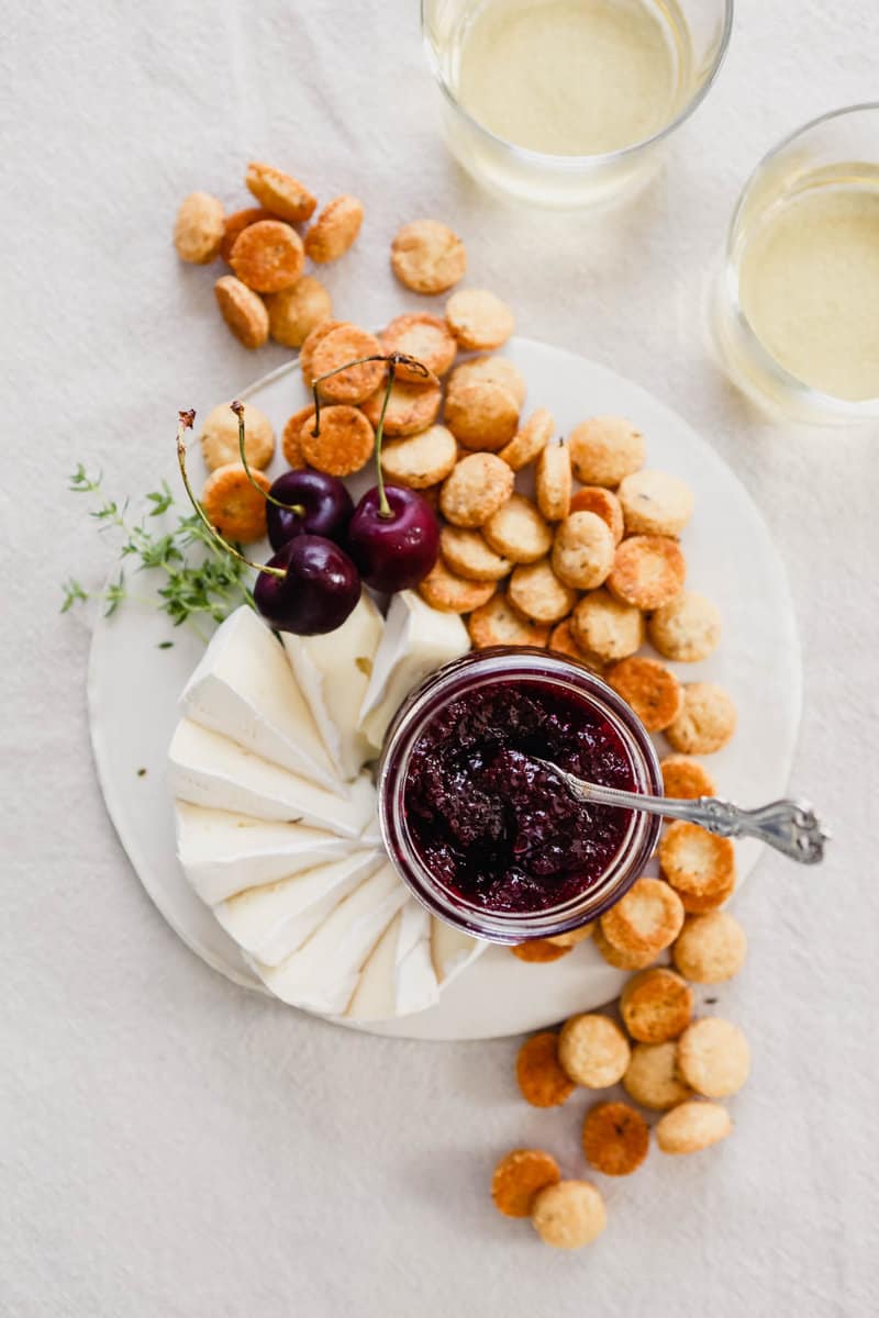 Overhead photograph of homemade cherry jam on a plate with crackers and cheese