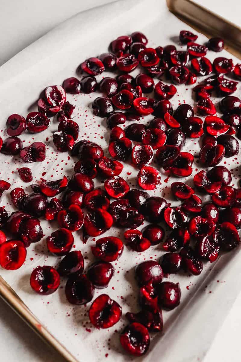 Photograph of halved fresh cherries on a baking sheet