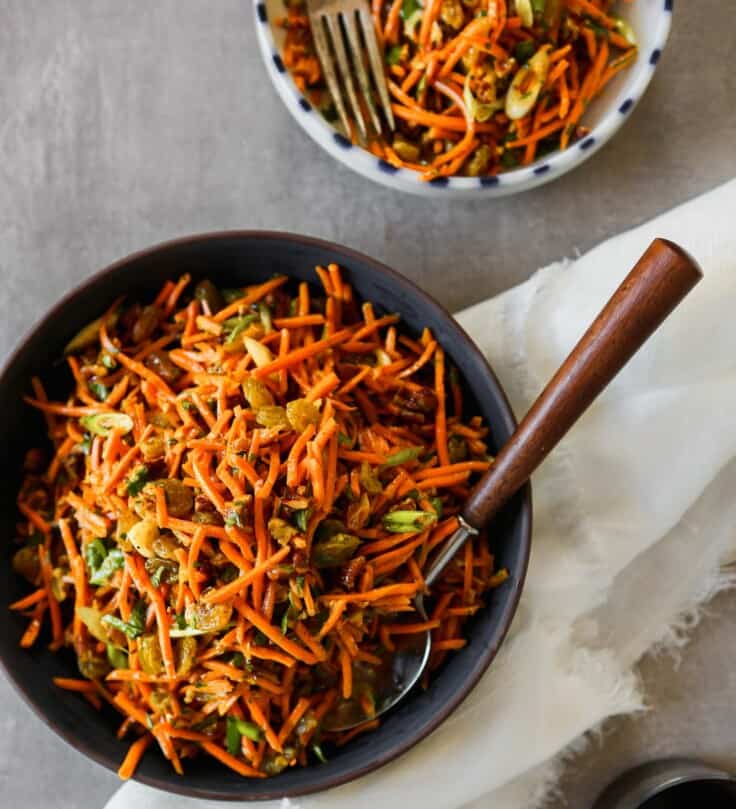 Photograph of shredded Moroccan carrot salad in a dark blue bowl set on a gray table.