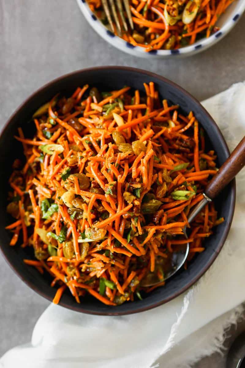 Photograph of shredded Moroccan carrot salad in a dark blue bowl set on a gray table.