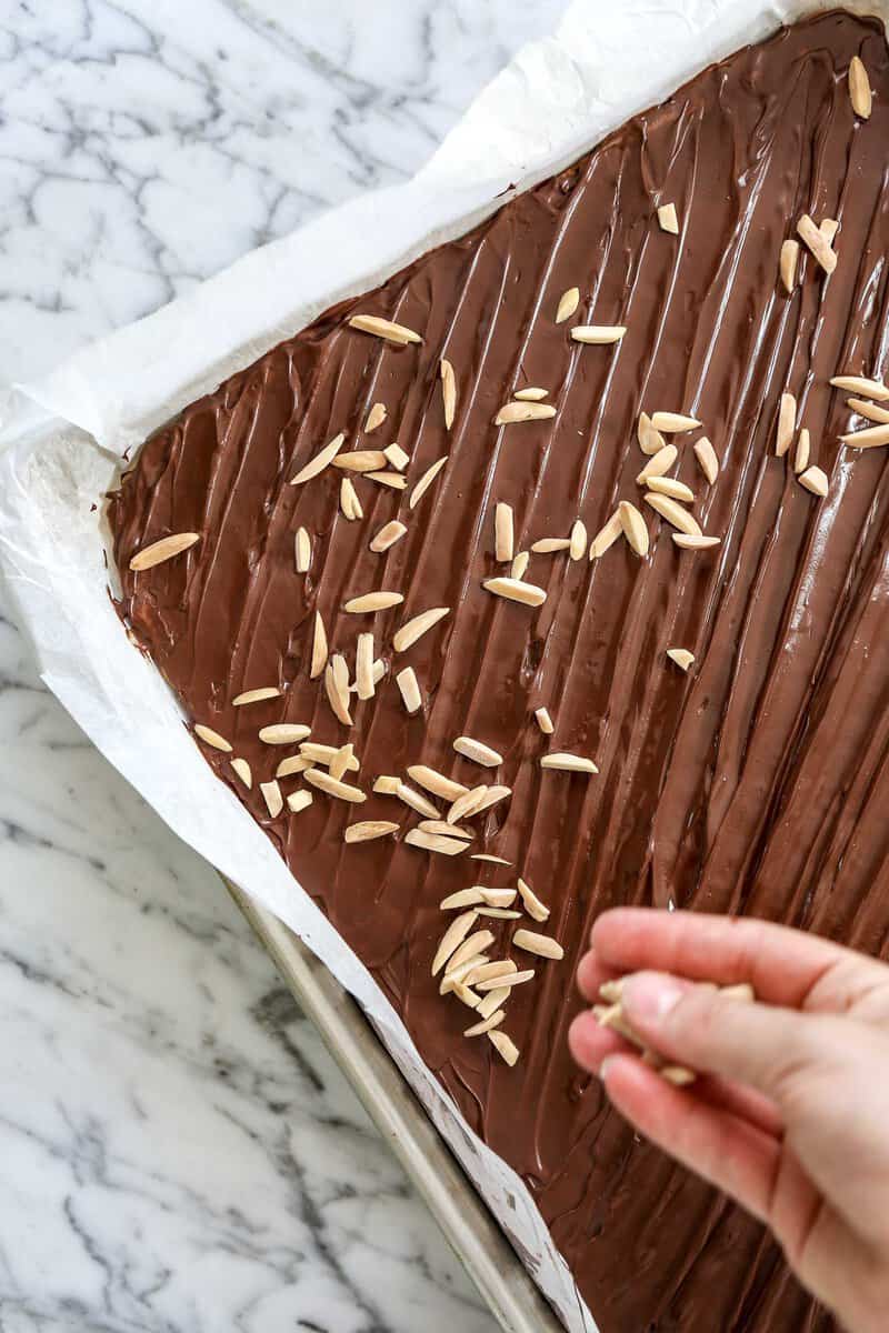 photo of almonds being sprinkled over chocolate layer on cookie bar