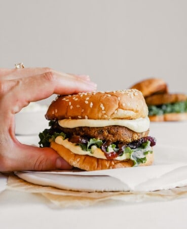 Photograph of someone picking up a vegan mushroom veggie burger on a white plate