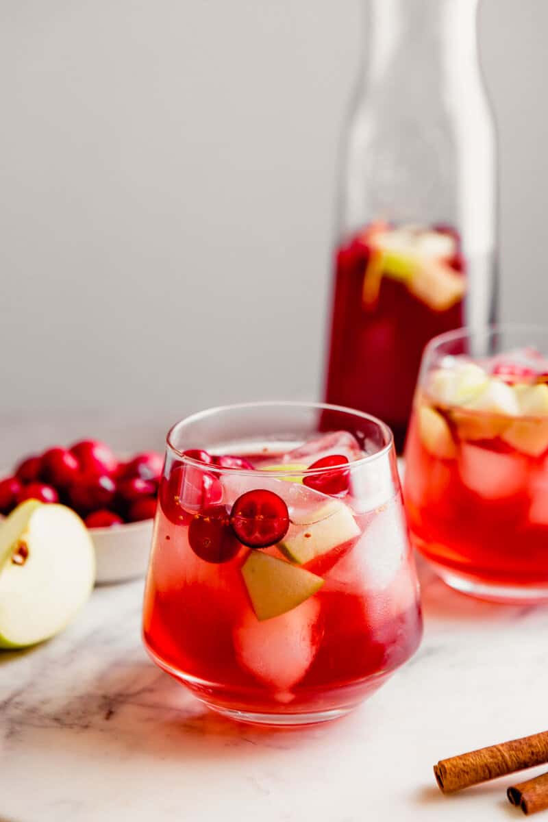 Photograph of two glasses of rose sangria set on a marble platter with a pitcher of sangria in the background.