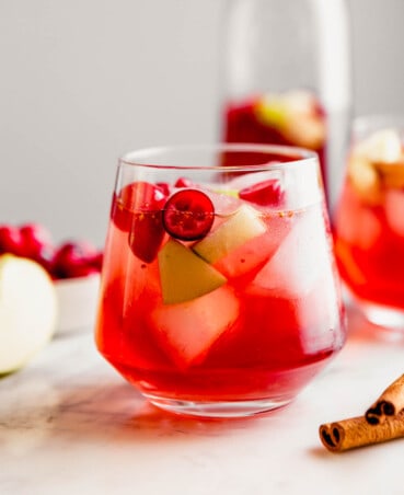 Close up Photograph of a cranberry sangria, featuring fresh cranberries and apple chunks, set on a marble platter.