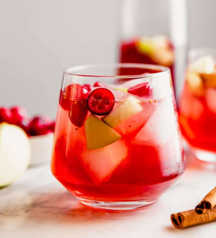 Close up Photograph of a cranberry sangria, featuring fresh cranberries and apple chunks, set on a marble platter.