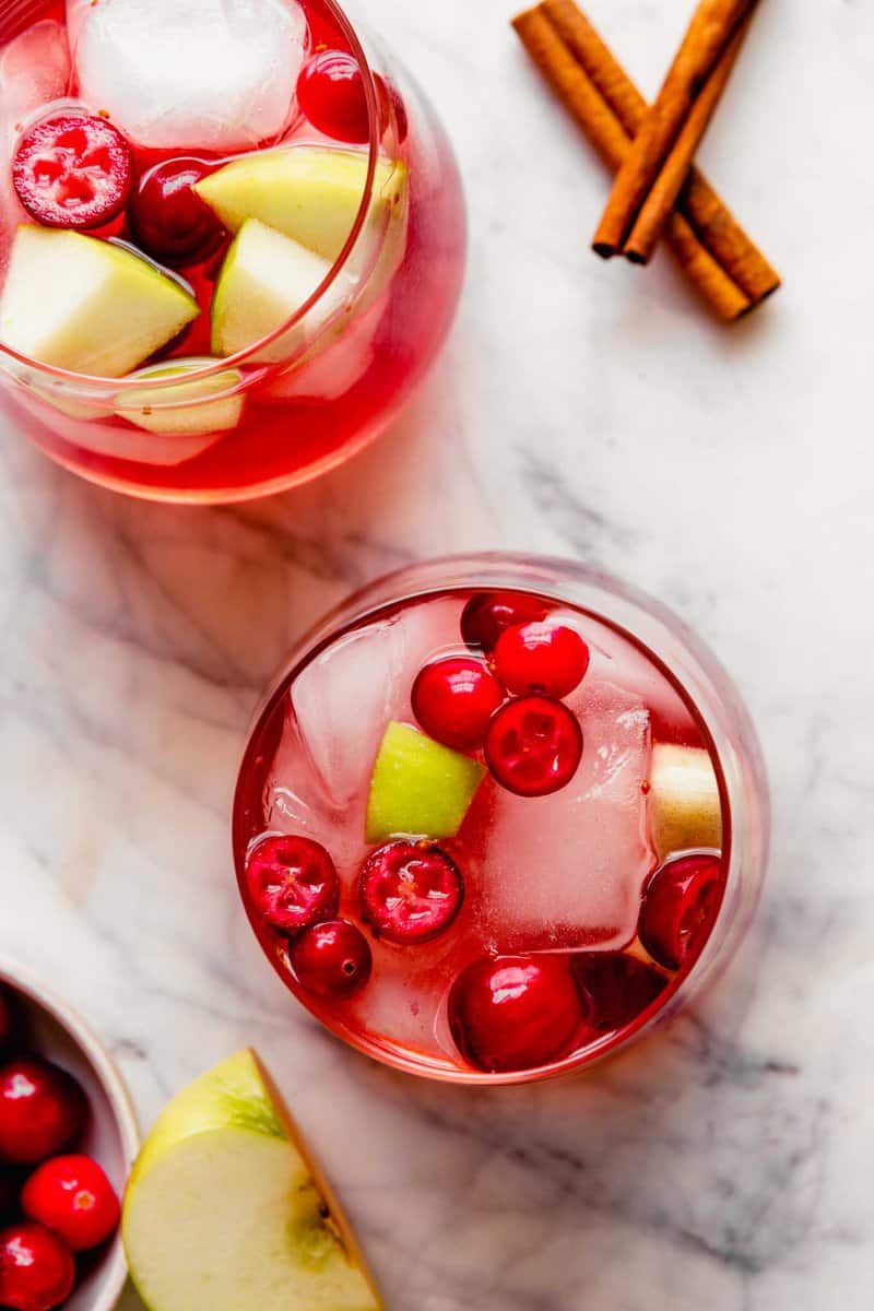 Overhead photograph of a fall sangria, featuring fresh cranberries and apple chunks, set on a marble platter.