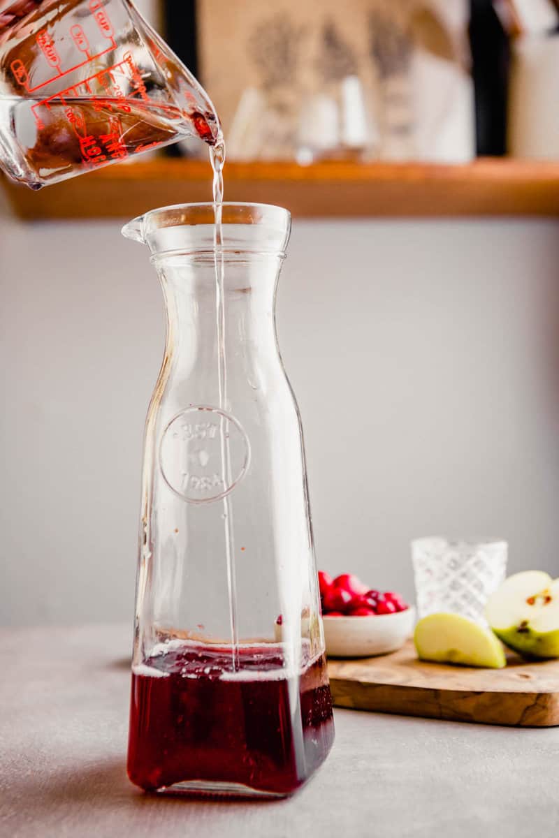 Photograph of vodka being poured into a pitcher with a cranberry simple syrup to make a fall sangria.