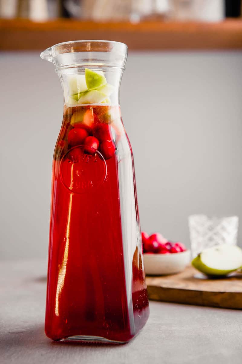 Photograph of a pitcher of rose sangria with fresh cranberries and chopped apples.