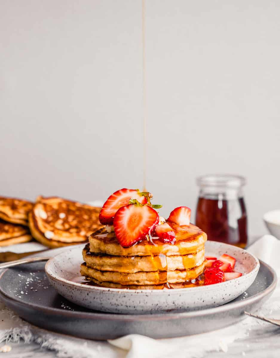 Photo of toasted oat pancakes stacked on a plate topped with butter, maple syrup and strawberries