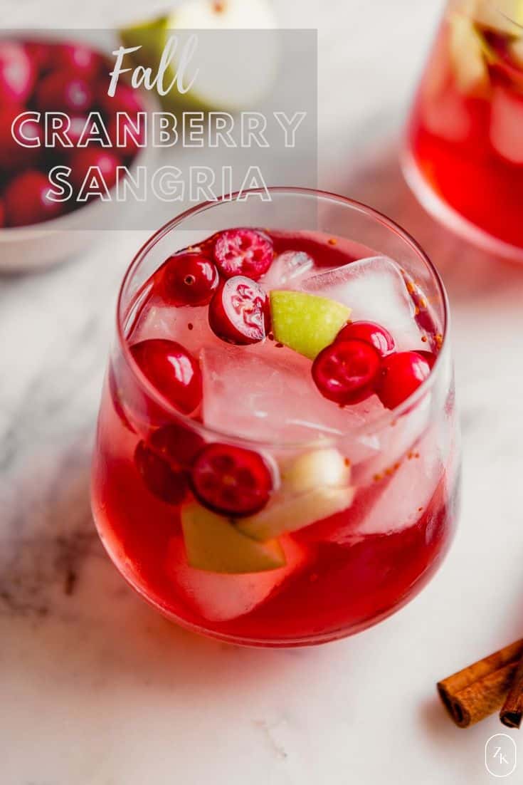 Overhead photograph of a fall sangria, featuring fresh cranberries and apple chunks, set on a marble platter with cinnamon sticks and more cranberries.