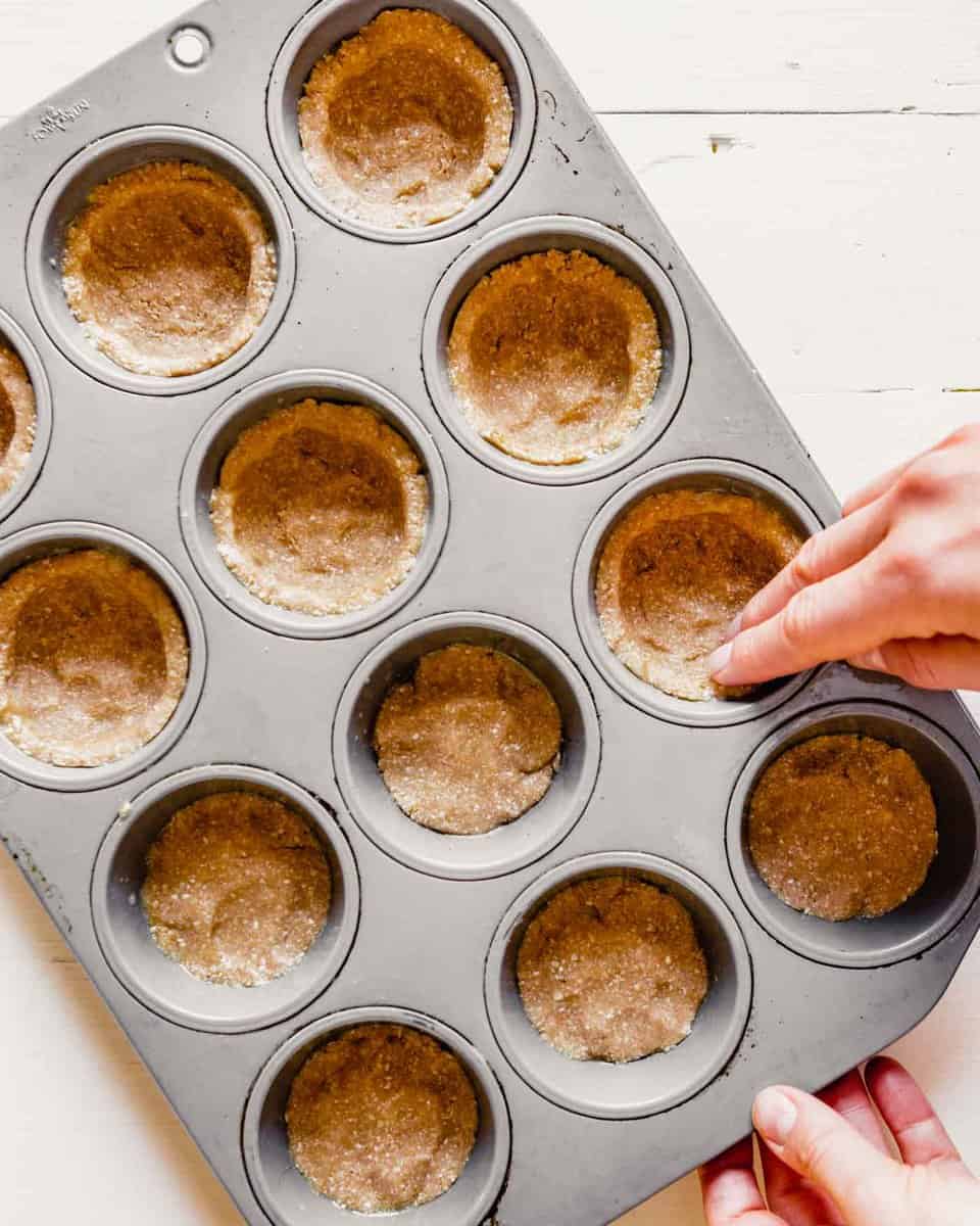 overhead image of dough being pressed into the bottom and up sides of a muffin tin