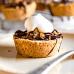 Side angle of a mini pecan pie topped with a dollop of whipped cream on a cream-colored plate