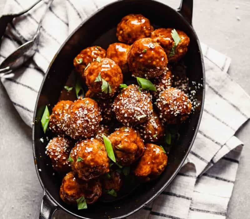 Overhead image of glazed turkey meatballs piled into an oval baking dish set on a stripped napkin.