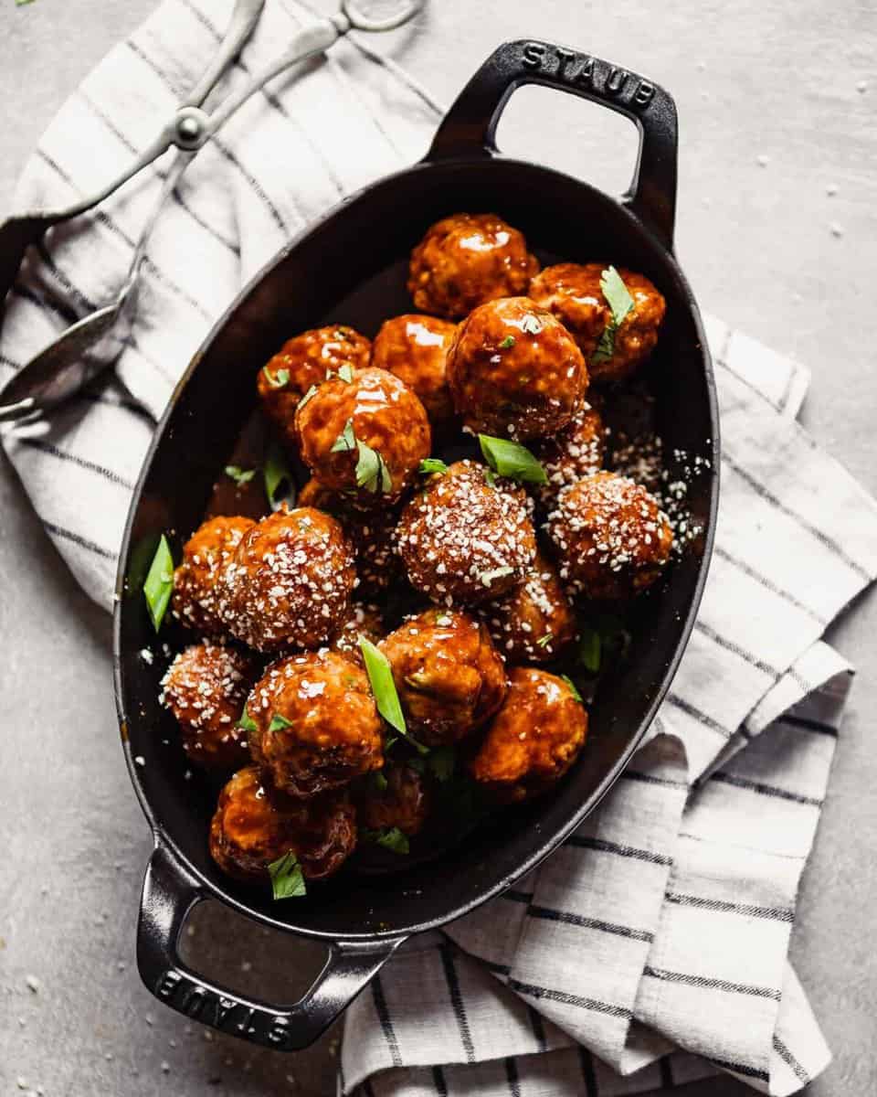 Overhead image of glazed turkey meatballs piled into an oval baking dish set on a stripped napkin.