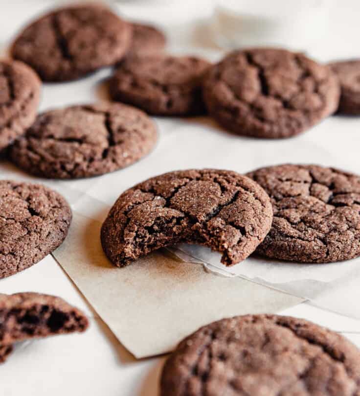 Side angle of a chewy chocolate cookie with a bite taken out of it arrange on a table with other cookies