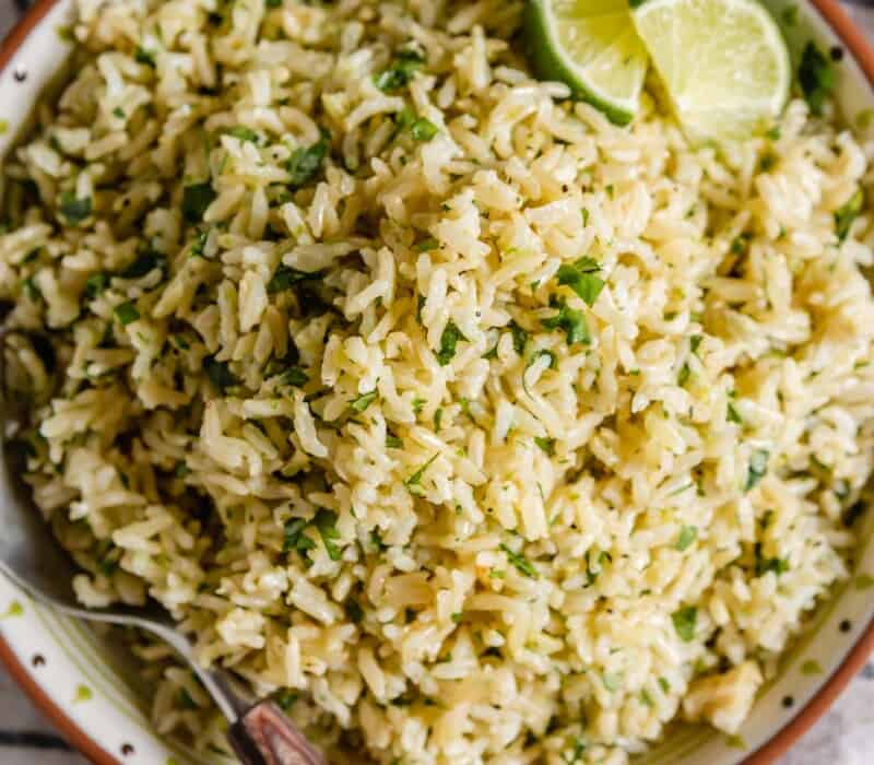 overhead image of brown rice with chopped cilantro and lime wedges in a shallow bowl