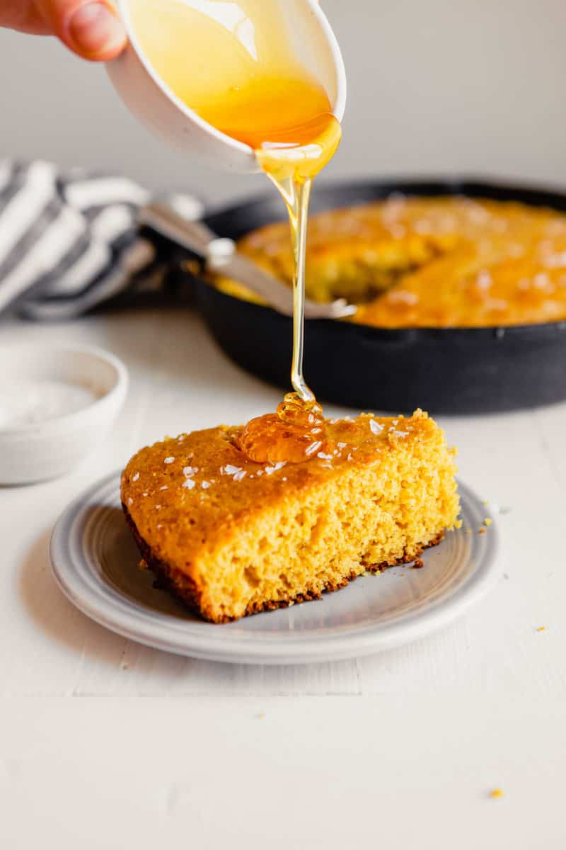 Side angle of a wedge of healthy cornbread with honey being drizzled over it 