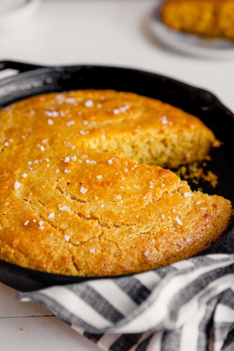 Side angle of cornbread in a cast iron skillet with a piece taken out
