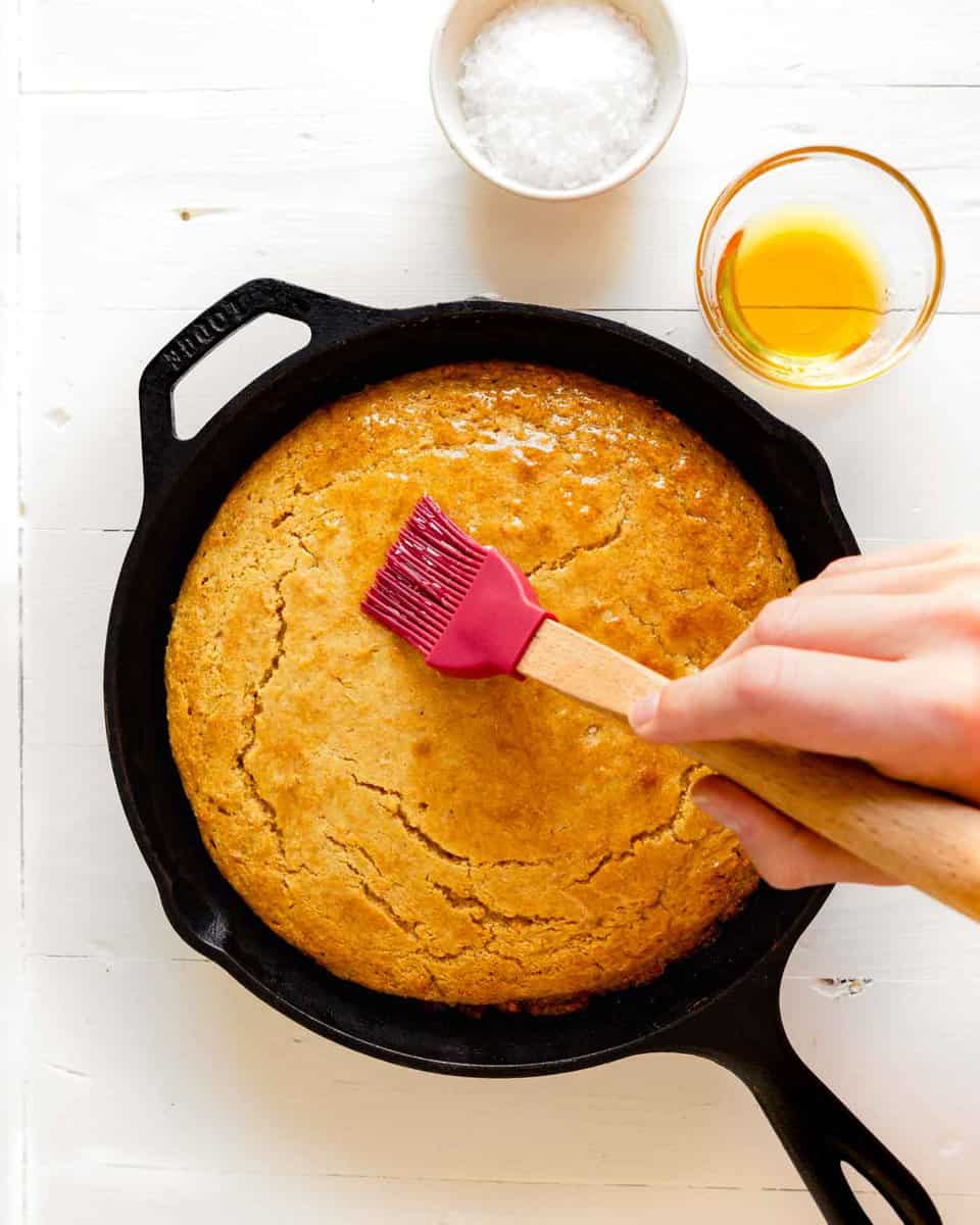 Overhead image of honey being brushed over cornbread in a cast iron skillet