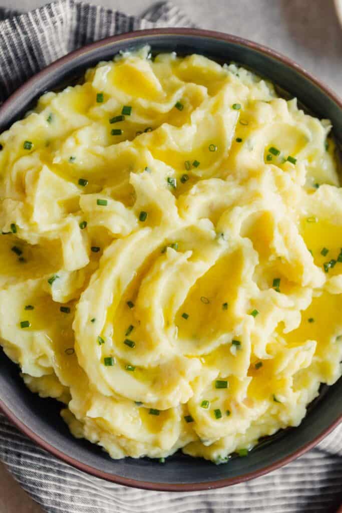 Overhead and closeup photo of creamy mashed potatoes in a blue bowl with chives on top
