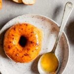 Close up image of glazed mochi doughnut on a speckled white plate with a spoon of glaze next to it