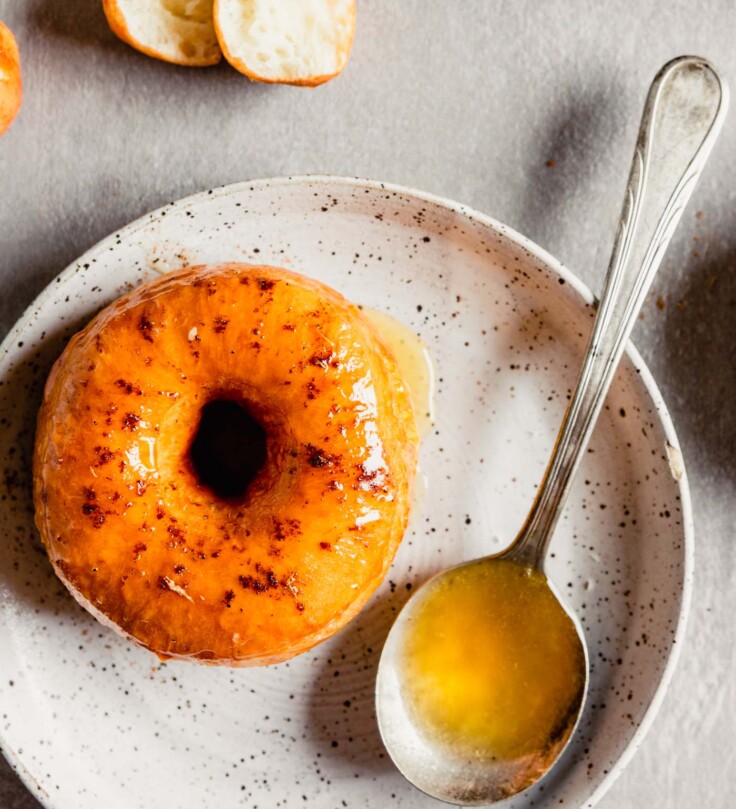 Close up image of glazed mochi doughnut on a speckled white plate with a spoon of glaze next to it