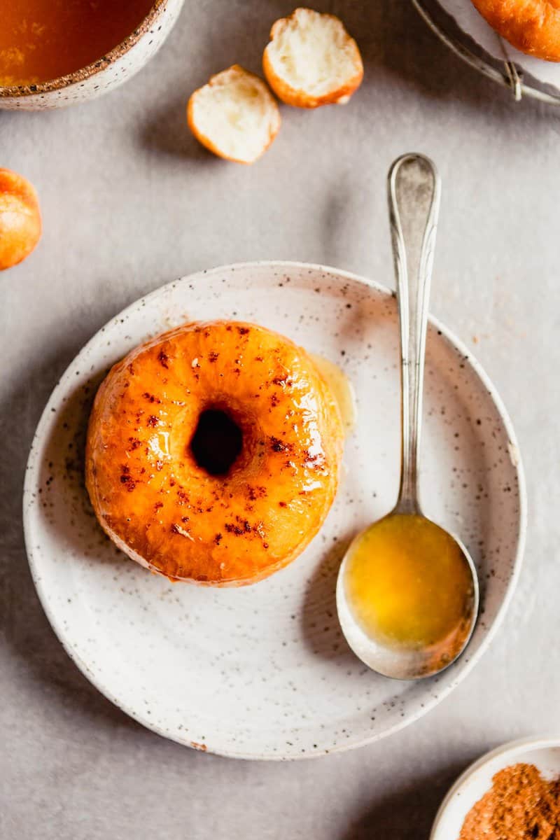 Overhead image of a glazed mochi donut on a white speckled plate with a spoon of glaze set off to the side.