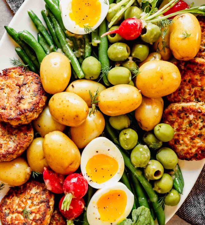 Overhead photo of nicoise salad on a white plate with salmon cakes arranged around the edges of the plate.