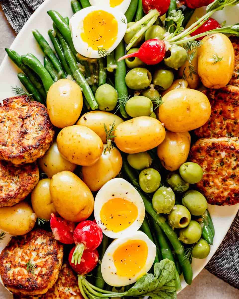 Overhead photo of nicoise salad on a white plate with salmon cakes arranged around the edges of the plate.