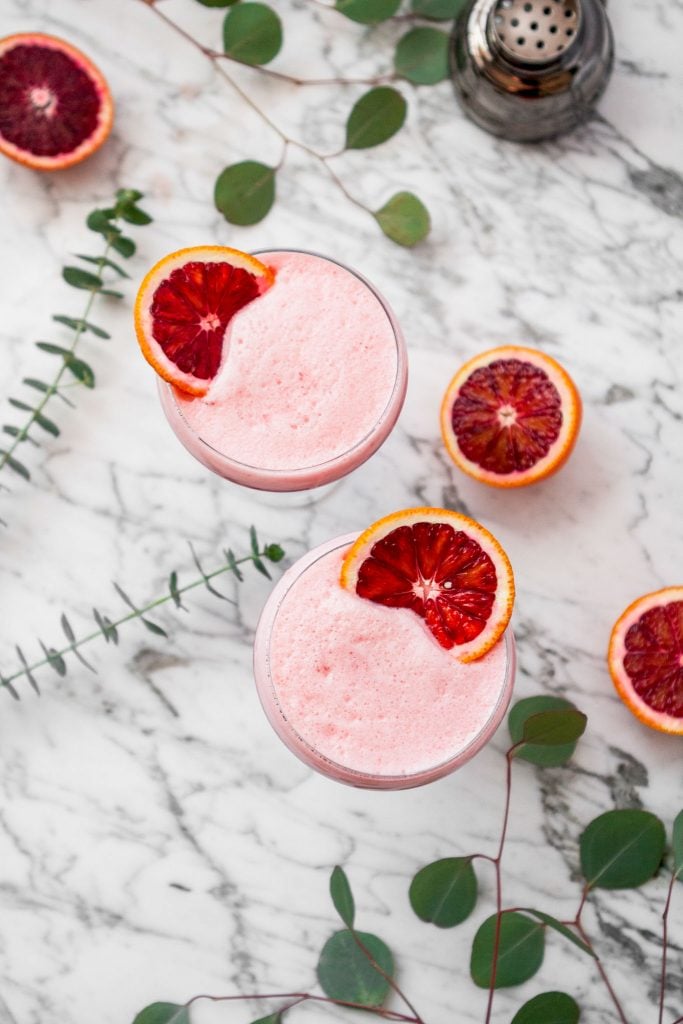 overhead image of foam-topped cocktails set on a white marble table with blood orange slices set on top