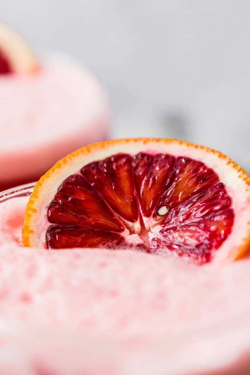 close up image of a blood orange slice on top of a foamy cocktail
