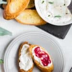 overhead image of a slate board topped with a bowl of whipped ricotta and toasted crostini. A plate with mini toasts topped with ricotta and curd off to the side