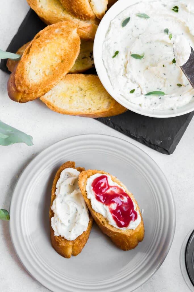 overhead image of a slate board topped with a bowl of whipped ricotta and toasted crostini. A plate with mini toasts topped with ricotta and curd off to the side