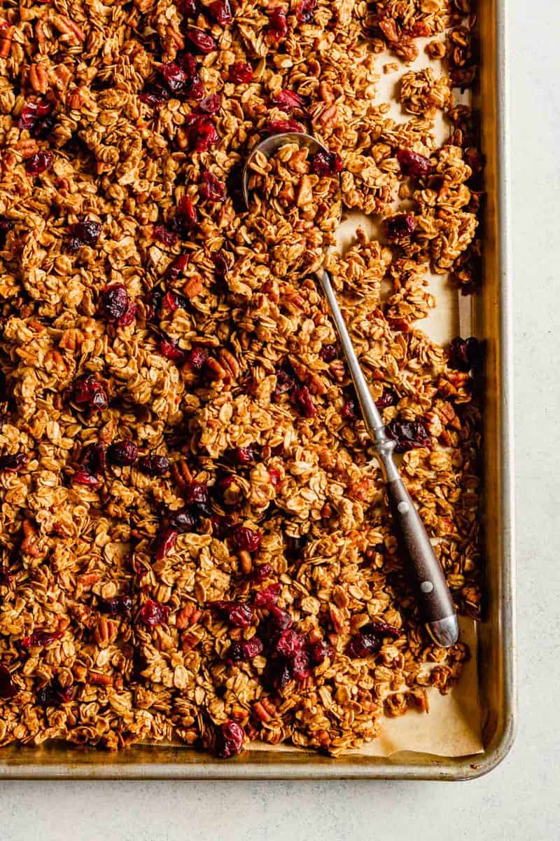 Overhead image of granola on a baking sheet with a spoon laid over top