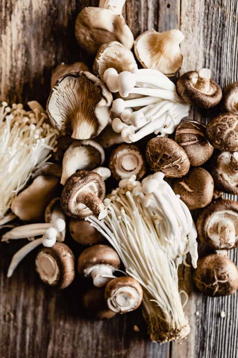 overhead image of various types of mushrooms piled onto a wood table