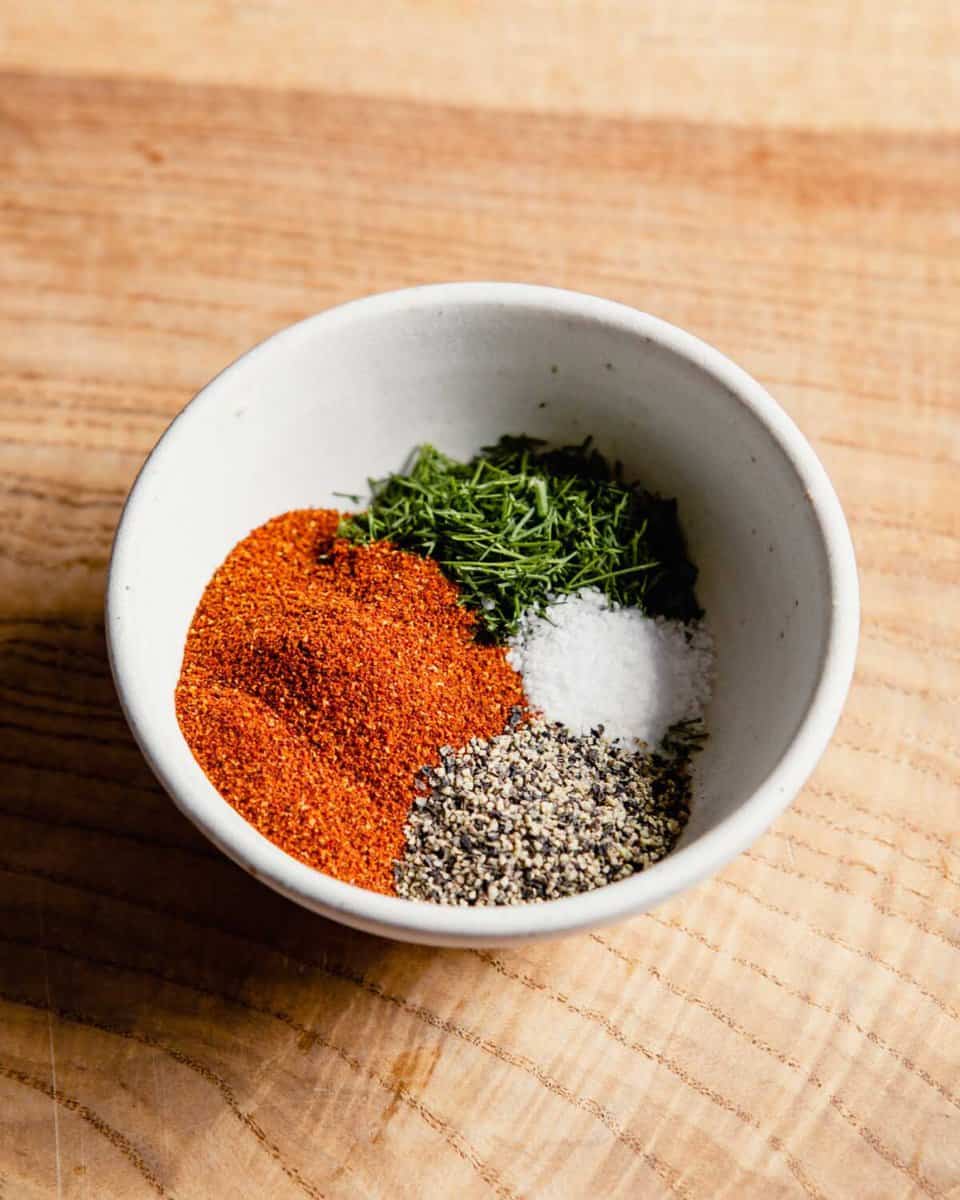 a small white bowl filled with paprika, salt, pepper and fresh dill