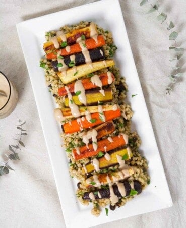Roasted Root Vegetables layered over a sorghum pilaf on a long rectangular white plate.