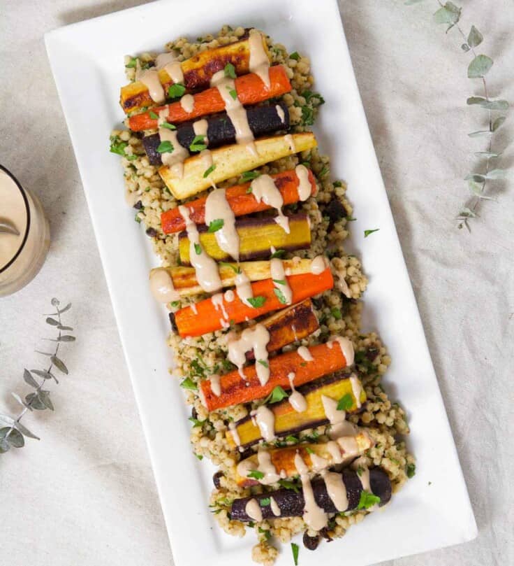 Roasted Root Vegetables layered over a sorghum pilaf on a long rectangular white plate.