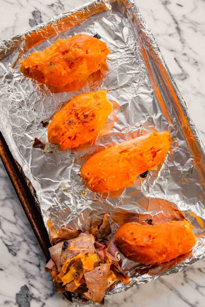 Overhead image of roasted  sweet potatoes being peeled on a foil-lined baking sheet 