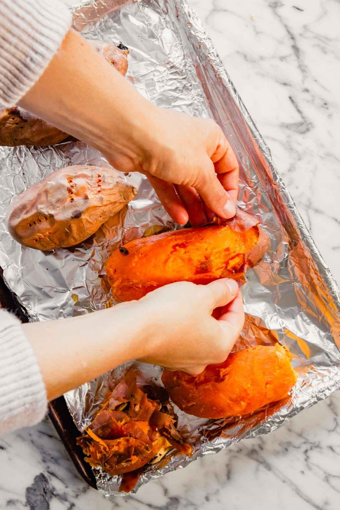 Overhead image of roasted  sweet potatoes being peeled on a foil-lined baking sheet 