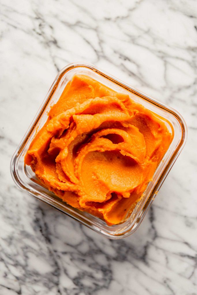 Overhead image of sweet potato puree in a glass container set on a marble table