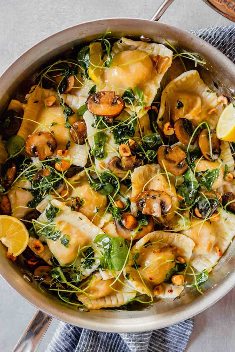 Overhead image of vegan ravioli in a saute pan with mushrooms and watercress