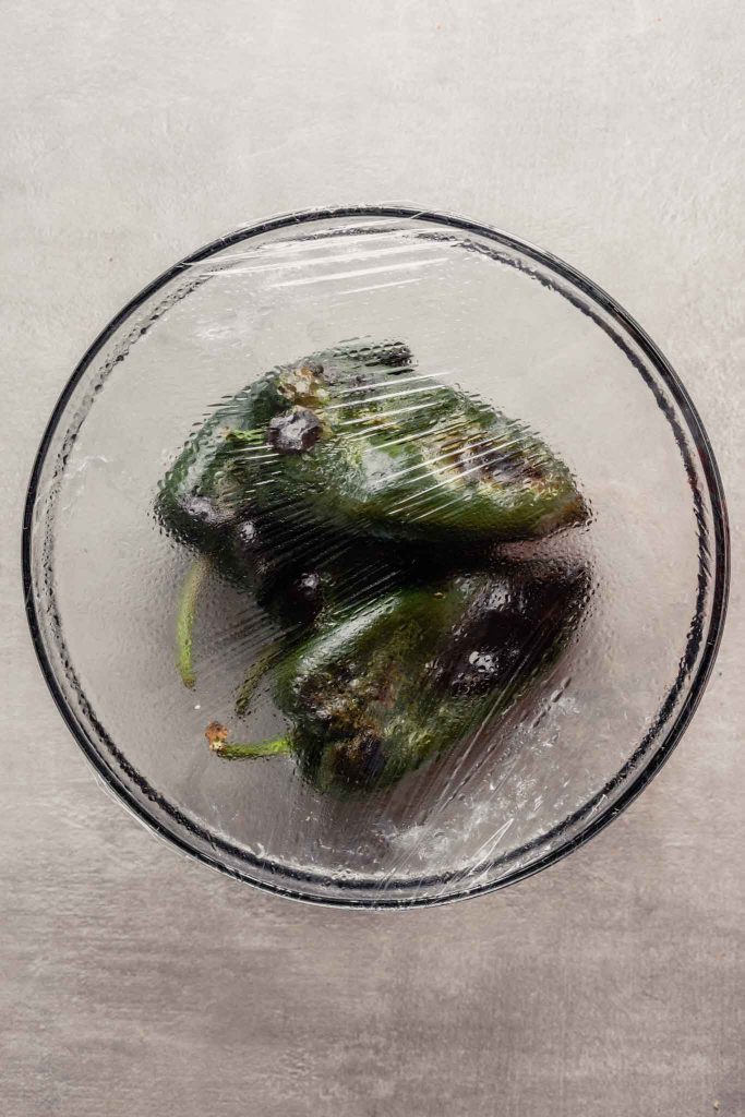 oberhead image of roasted poblano peppers in a bowl covered with plastic wrap