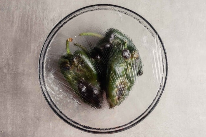 oberhead image of roasted poblano peppers in a bowl covered with plastic wrap