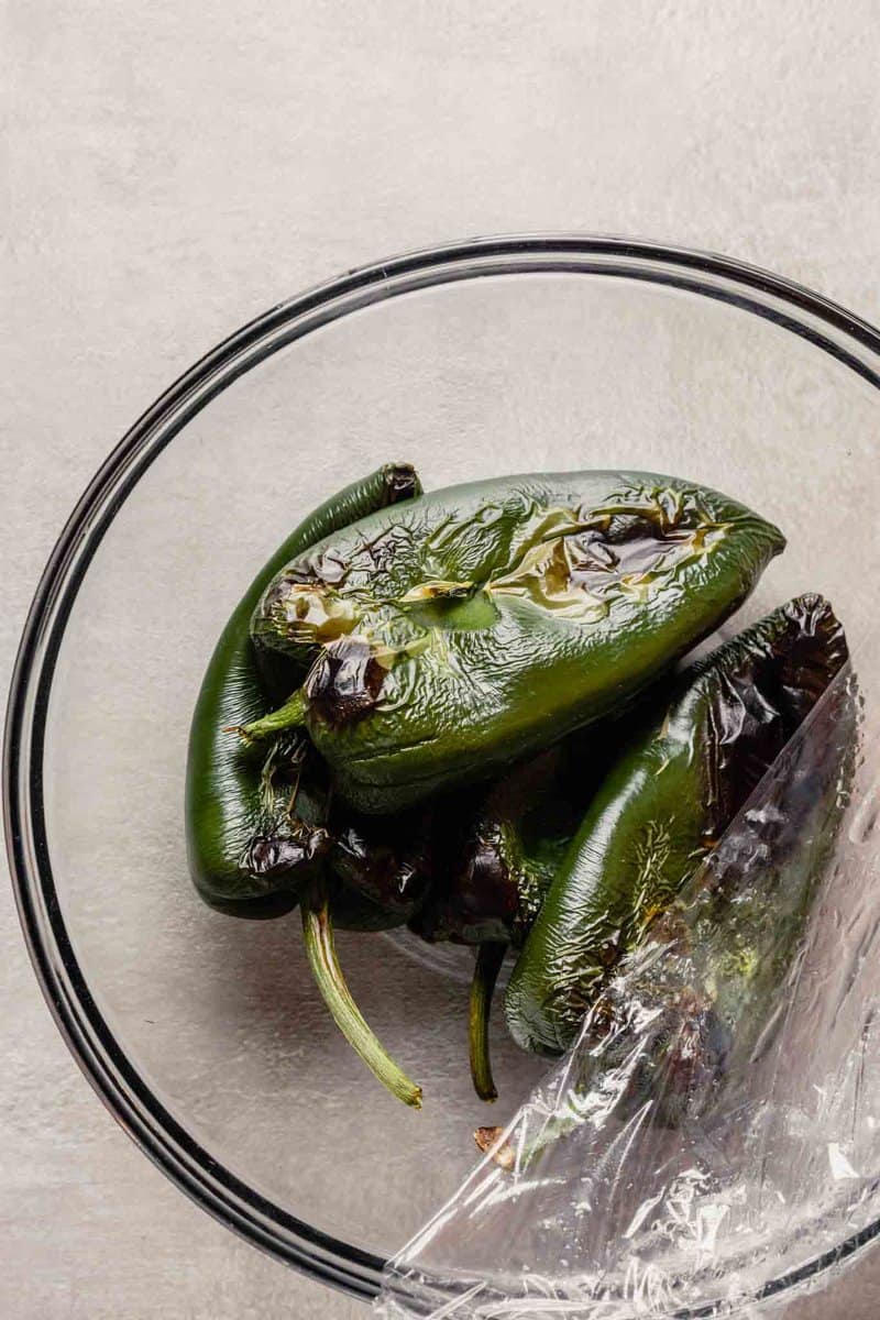 Overhead image of roasted and steamed poblano chiles in a glass bowl